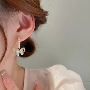 Dettaglio di orecchini a fiocco dorati con perle e strass indossati da modella