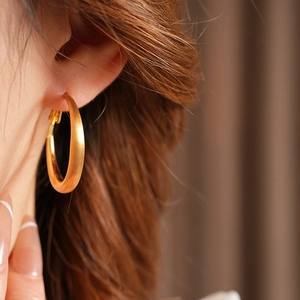 Close-up of a matte gold geometric hoop earring worn by a model in a luxury setting