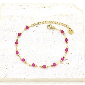 Macro detail of gold-plated bracelet with magenta stone beads and adjustable chain clasp