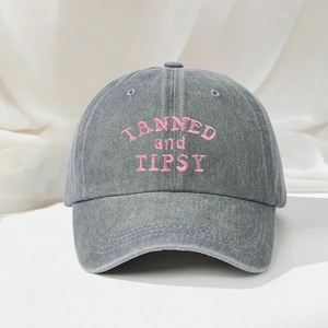 Detailed view of pink TANNED and TIPSY letter embroidery on washed grey denim baseball cap