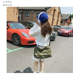 Street style shot of army green canvas messenger bag worn with a casual white shirt