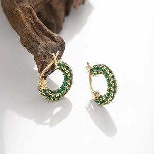 Elegant gold huggie hoop earrings with micro-paved green zircon stones on wood background