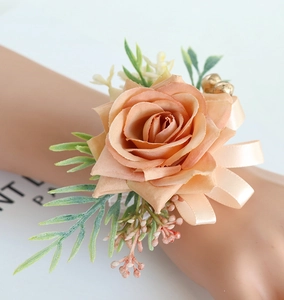 Close-up of a pale apricot artificial rose wrist corsage with green leaves and ribbon