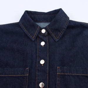 Détail d'une chemise en jean indigo avec surpiqûres orange et boutons en métal argenté