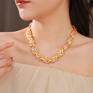Close-up of a vintage leaf-shaped golden pearl necklace worn by a model on a beige dress