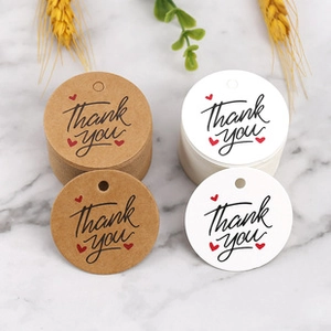 Close-up of kraft and white round Thank You tags with red hearts on marble background
