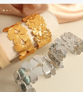 Detailed close-up of 18K gold plated butterfly and flower embossed steel cuff bracelets