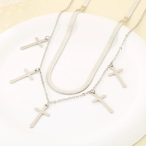 Detail of silver double-layered necklace featuring cross pendants and snake chain on ceramic