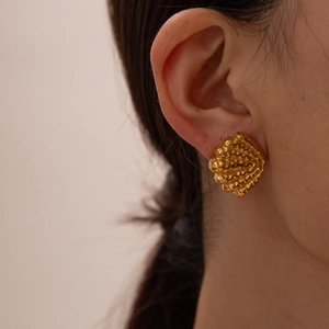 Golden shell-shaped stainless steel stud earring shown as a close-up on a model's ear