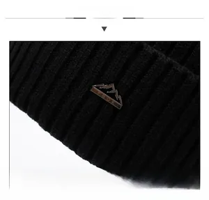 Macro shot of black ribbed knit beanie featuring a metal mountain logo and fine texture