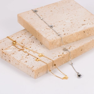 Elegant stainless steel butterfly anklets in gold and silver on beige travertine
