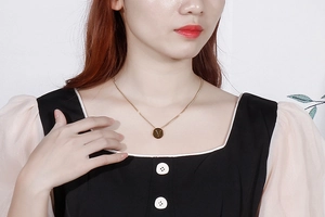 Detail of a gold titanium steel necklace with a round letter V pendant on a female model