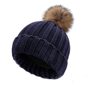 Thick navy blue cable knit winter hat with a fluffy faux fur pompom and cuffed rim