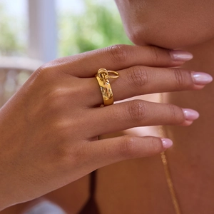Gold stainless steel wide band ring with interlocking buckle charm on model hand