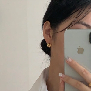 Primo piano di orecchini a nodo intrecciato dorato indossati da una modella in camicia