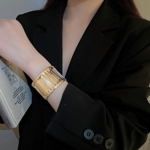 Macro detail of a wide gold metal striped cuff bracelet on a woman in black suit