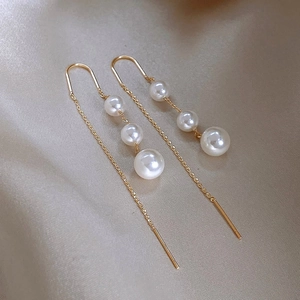 Elegant gold long tassel earrings with white pearls on premium champagne satin background