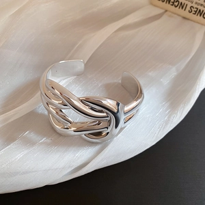 Macro shot of wide silver liquid metal knot cuff bracelet on soft silk fabric
