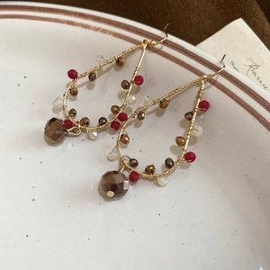 Close-up of handmade gold metal drop earrings with colorful beads and crystal pendant