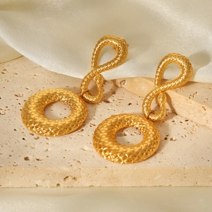 Détail de boucles d'oreilles serpent en or 18K avec cercles texturés sur fond de soie beige