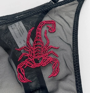 Detailed macro view of red scorpion embroidery on sheer black mesh lace fabric