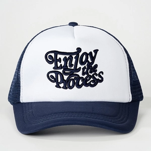 Gros plan de la broderie Enjoy the process sur casquette trucker bleue et blanche