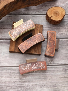 Detailed close-up of western leather hair claws with sunflower patterns and rivets