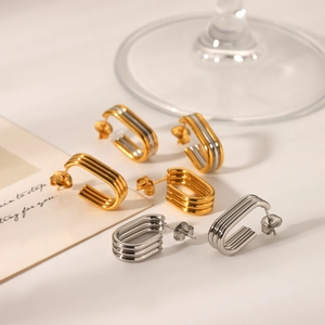 Three-layer curved stud earrings in gold and silver finishes on elegant glass display
