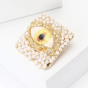 Golden alloy square brooch with cream pearls and evil eye design on geometric display