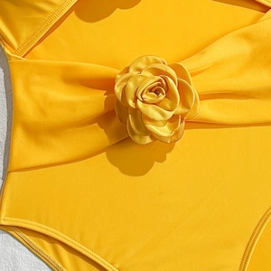 Detailed view of the bright yellow fabric and 3D floral accent on the one-piece swimsuit