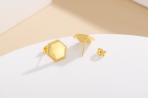 Macro detail of golden hexagonal stud earrings with beaded edges on textured background