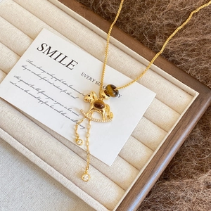 Detailed close-up of golden rocking horse necklace with tiger eye stones and zircon pendants