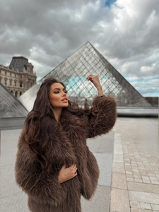 Detailed texture of thick dark brown faux fur jacket worn in a Paris street style setting