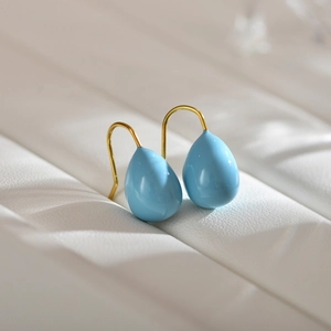 Elegant light blue water-drop earrings with gold hooks on white leather background