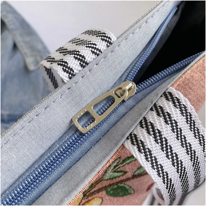 Detail of floral jacquard tote bag with metal zipper and striped webbing handle