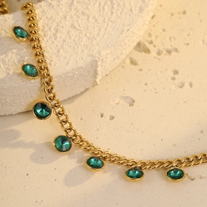 Macro shot of gold-plated stainless steel chain with seven faceted green crystals