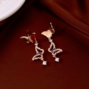 Detail of gold butterfly earrings with purple zircon stones on brown silk background