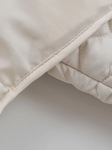 Detailed close-up of cream quilted jacket fabric showing fine stitching and smooth texture