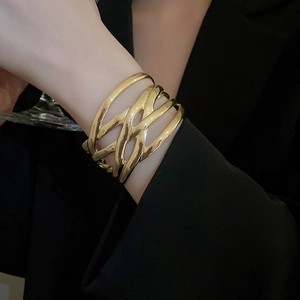 Close-up of irregular woven wide metal bangle in bright gold finish on a model wrist