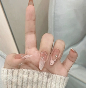 Detail of almond-shaped nails with pink gradient, bow patterns and rhinestone accents