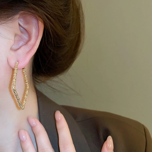 Close-up of model wearing gold geometric diamond-shaped earrings with textured finish