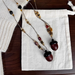 Ethic beaded necklace with acorn pendant and natural wood beads on white fabric