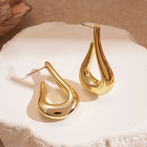 Macro detail of glossy gold drop earrings on a natural white stone surface with wood accents