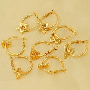 Detail of 18K gold hoop earrings with star and heart charms on silk fabric background