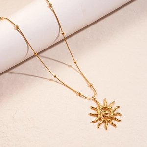 Detail of golden sun pendant with spiral texture on a dainty beaded snake chain necklace