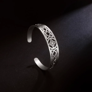 Detailed close-up of a silver Celtic knot cutout cuff bracelet on a black textured background