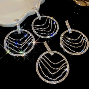 Détail de boucles d'oreilles rondes argentées avec pompons et chaînes de cristaux