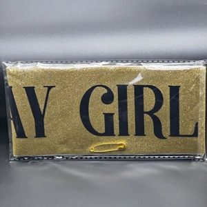 Detail of gold glitter birthday sash with AY GIRL text and safety pin in packaging