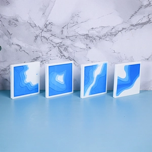 Detail of four square resin ocean wave coasters with blue layered texture on marble