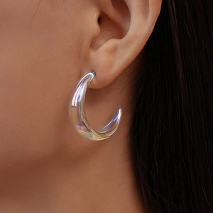 Close-up of a large iridescent acrylic C-hoop earring worn by a model in soft lighting